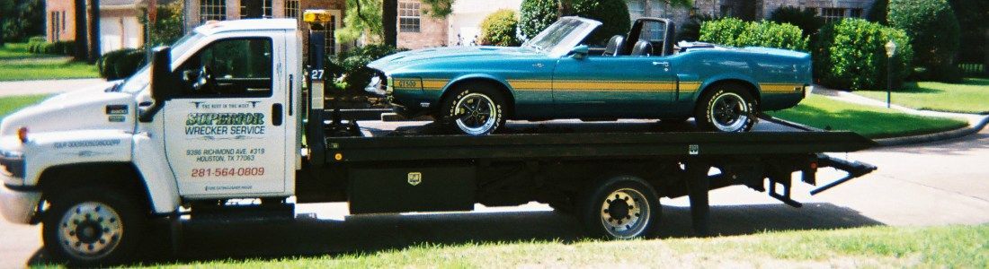 A teal convertible car being towed by a white tow truck