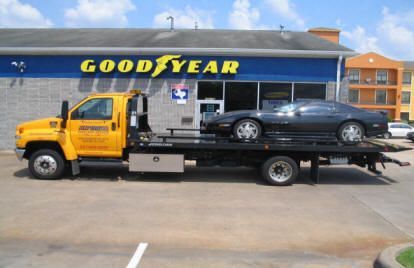 Yellow tow truck with a black car on its flatbed