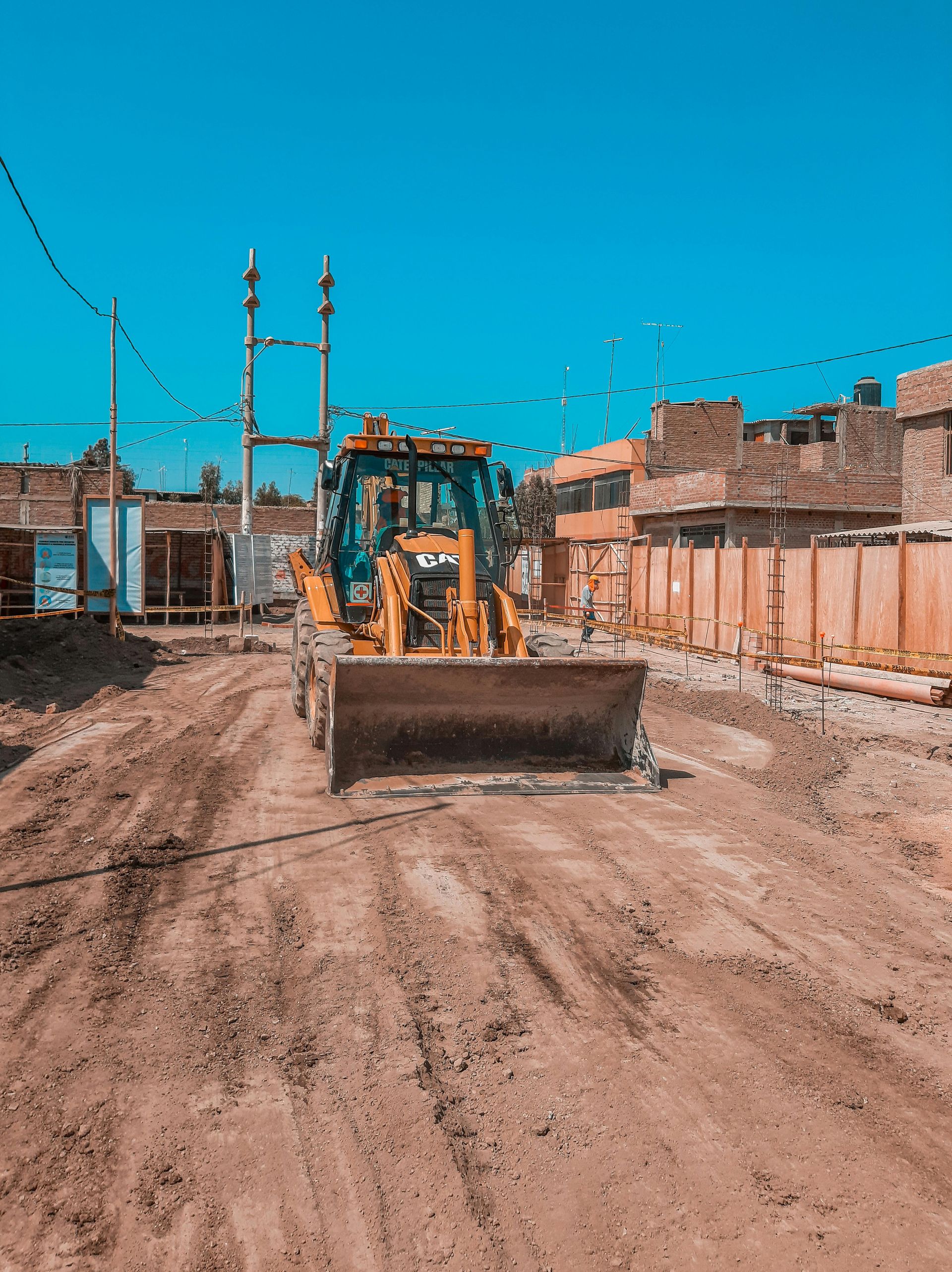 A yellow front-end loader sits on a dirt construction site under a clear blue sky, facing the camera.