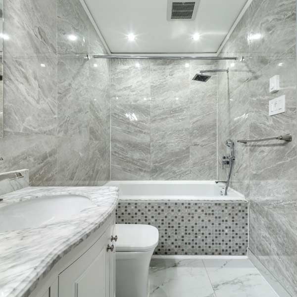 Bathroom renovation with marble-look walls, a bathtub with mosaic tile, and a white vanity.