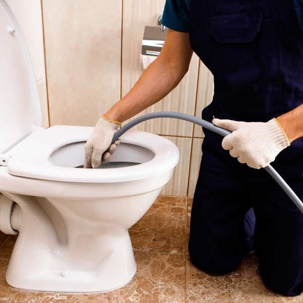 A Handyman unclogs a toilet with a snake in a bathroom.