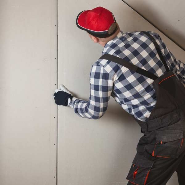 Man in overalls and a red cap, applying drywall compound to a wall Drywall Installation and Repair