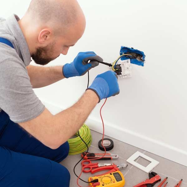 Man wearing blue gloves repairing an electrical outlet for Electrical Repair Services