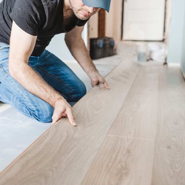 Contractor installing laminate flooring; light wood planks, blue jeans, casual clothing.