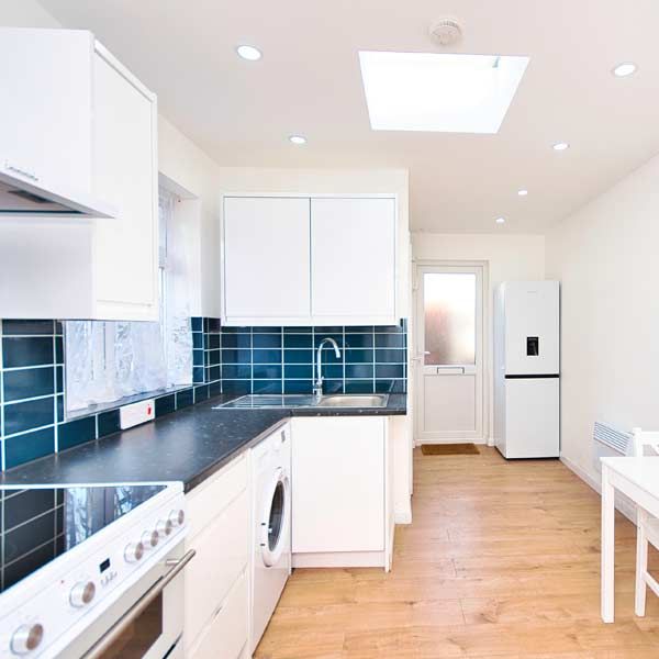 Garage Conversion with a White kitchen with blue tile backsplash, skylight, and light wood floors.