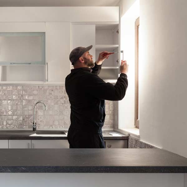 Home Improvement contractor, in a black uniform, fixing a kitchen cabinet with a screwdriver.