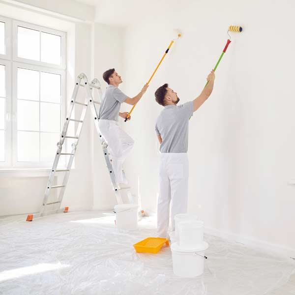 Two painters in white overalls use rollers on white walls, one on a ladder Interior Painting Services