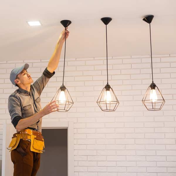 Handyman in cap installs light fixture, near two others. White brick wall.