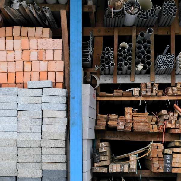 Shelves stocked with building materials including bricks, pipes, and lumber; viewed indoors.