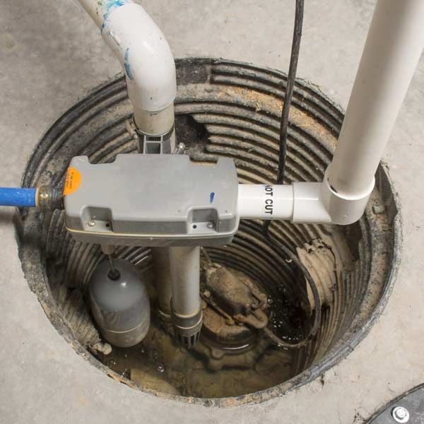 Sump pump repair in a concrete pit with pipes and float switch, partially submerged in water.