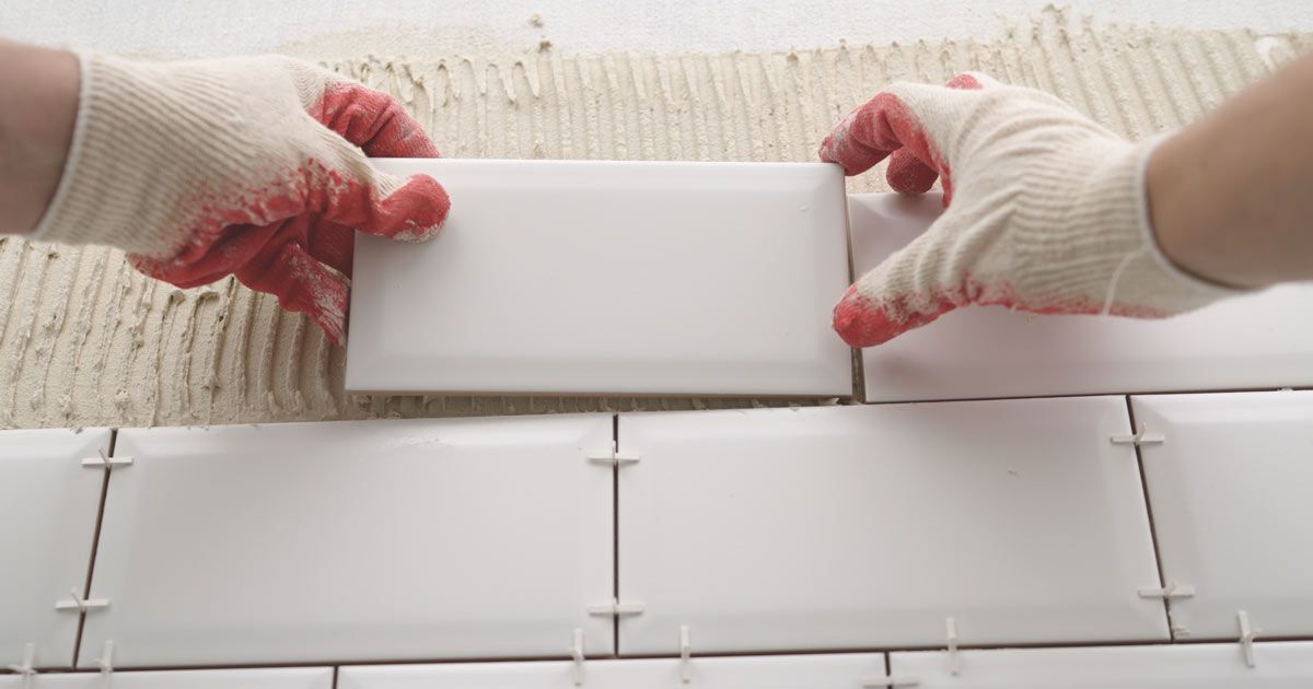 Hands in gloves placing white subway tiles with spacers on a wall by Tile Contractor Nassau County Honest Hammer Handyman