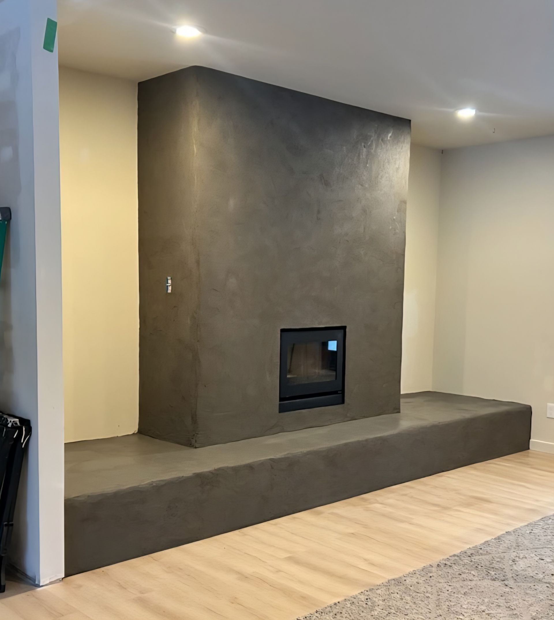 A modern fireplace featuring a dark, textured plaster surround and a raised hearth in a room with light wood floors.
