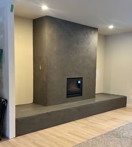 A modern charcoal-colored concrete fireplace surround and raised hearth against a light-colored wall.