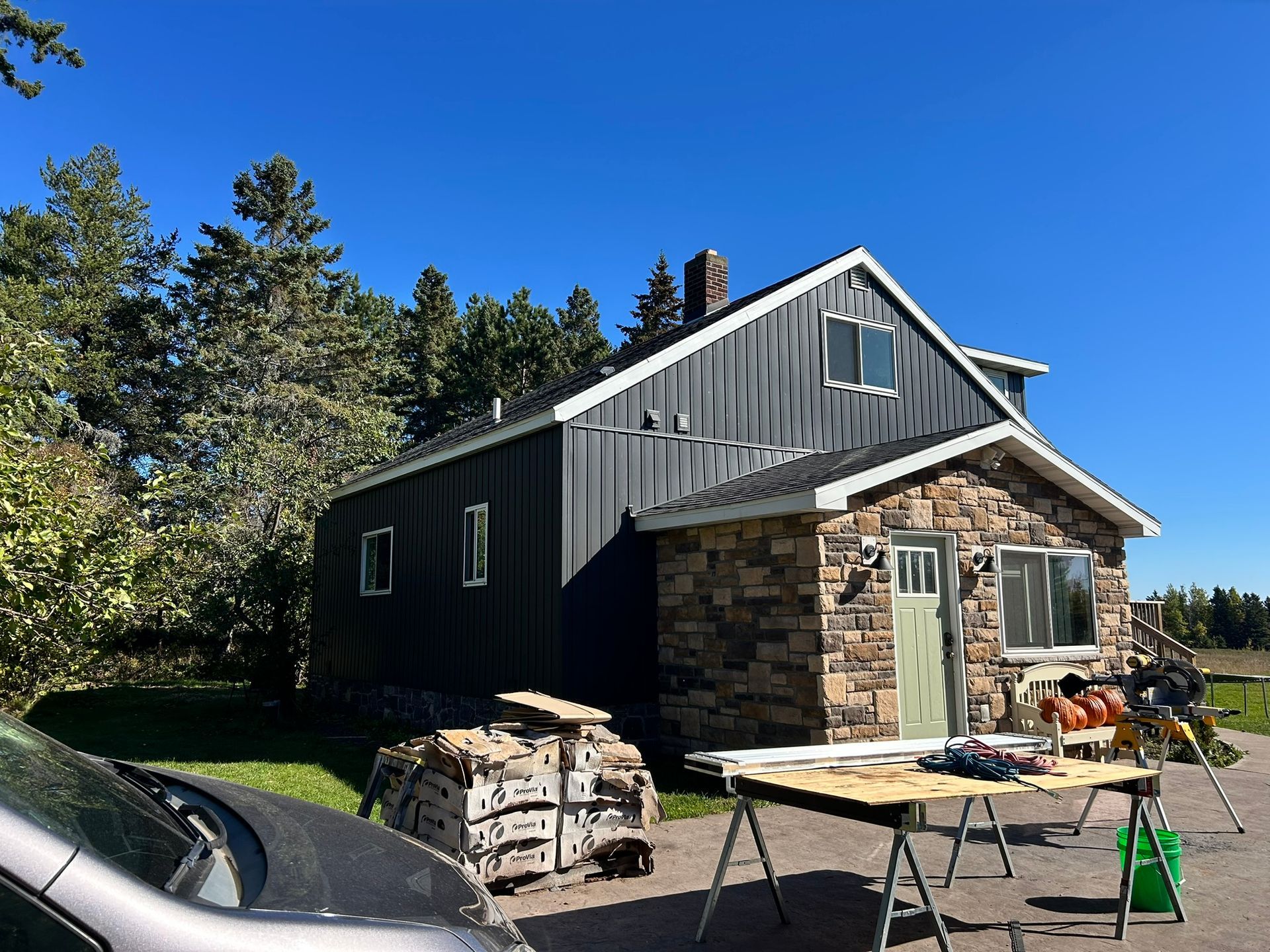 A renovated home with dark vertical siding and a stone front, featuring a workspace with construction tools outside.