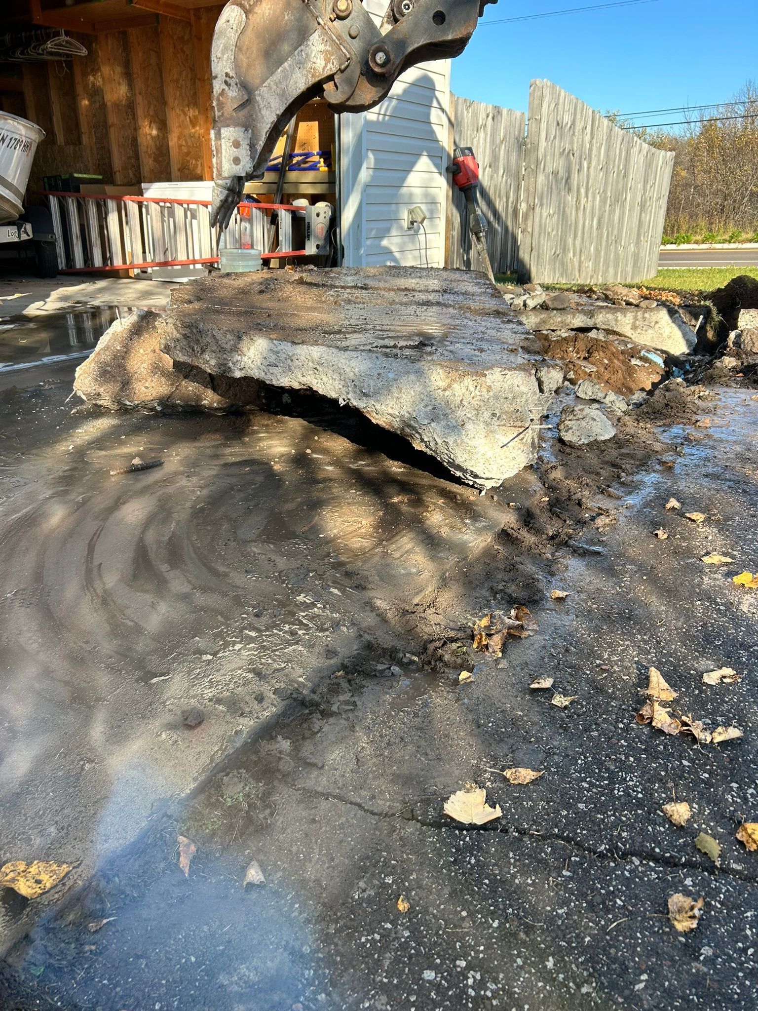 A construction excavator bucket lifting a large slab of broken concrete in an outdoor work site.