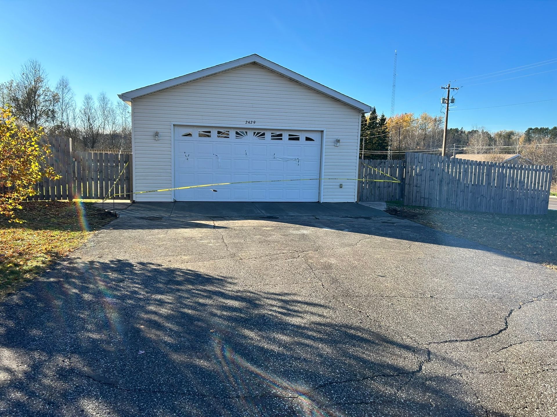 A white detached garage with a white sectional door faces a gravel driveway under a clear blue sky.