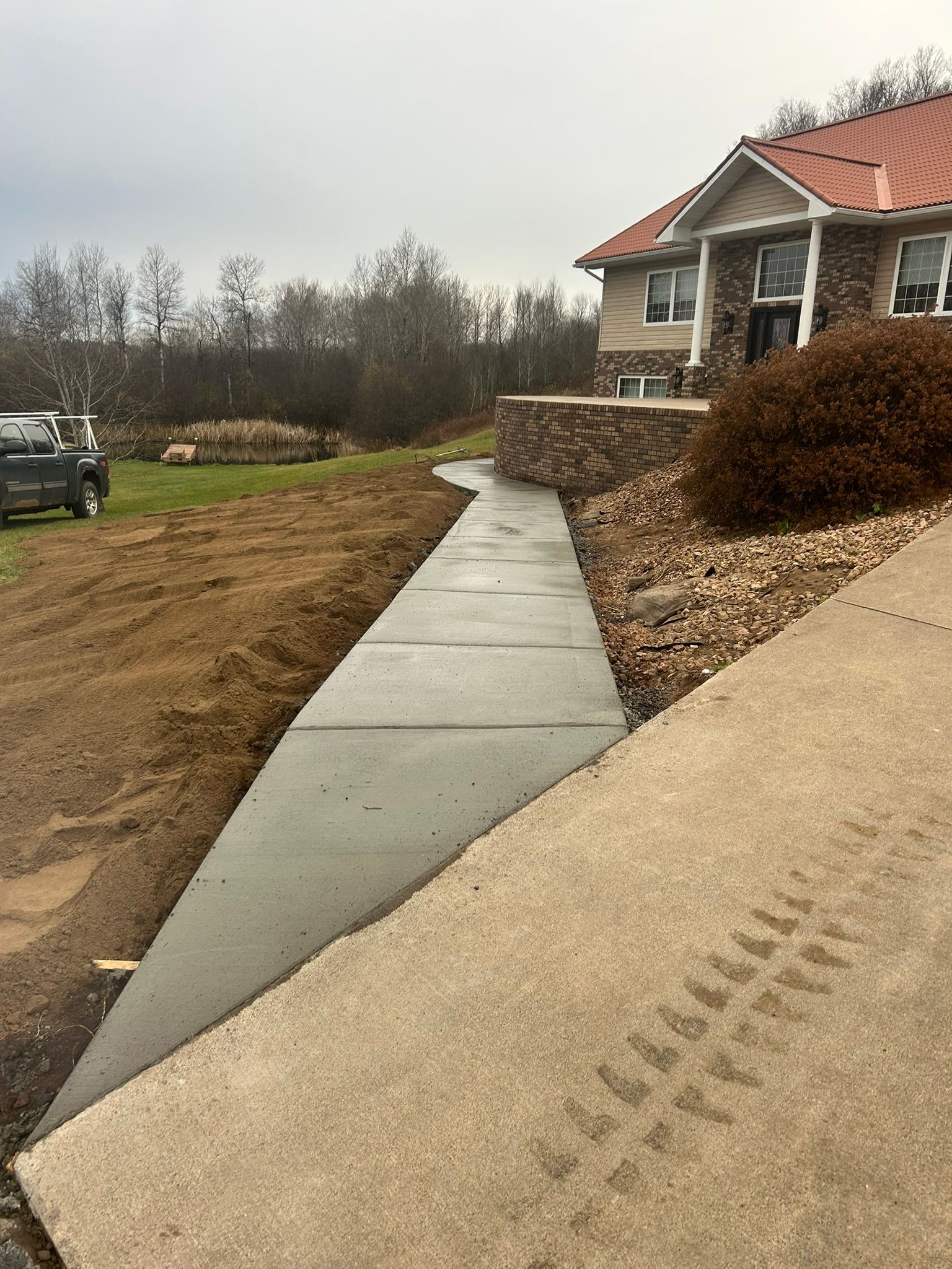 A newly poured concrete walkway runs alongside a house with a stone retaining wall and a large gravel bed.
