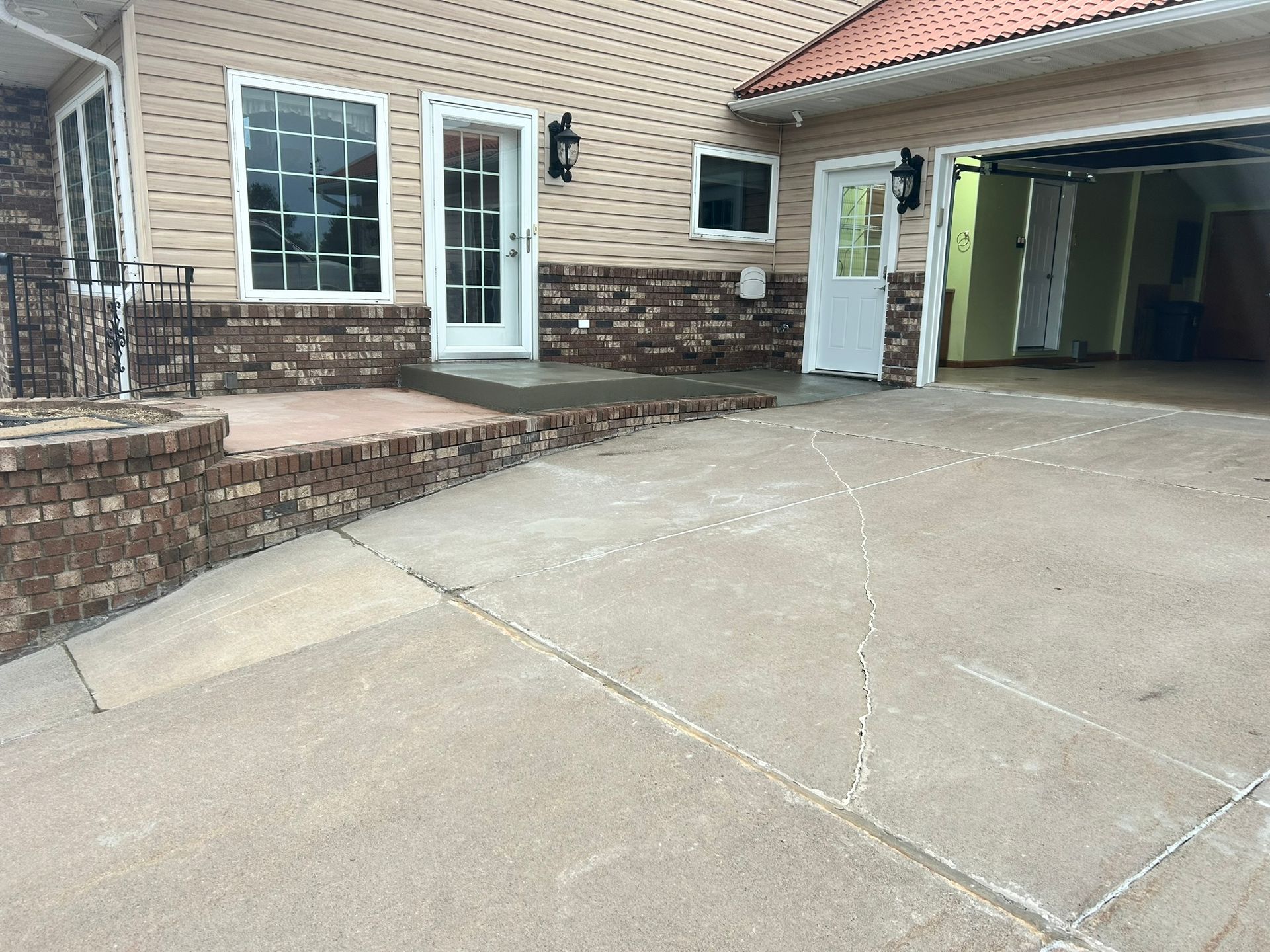A paved driveway leading to a house with beige siding, brick accents, a white door, and an open garage.