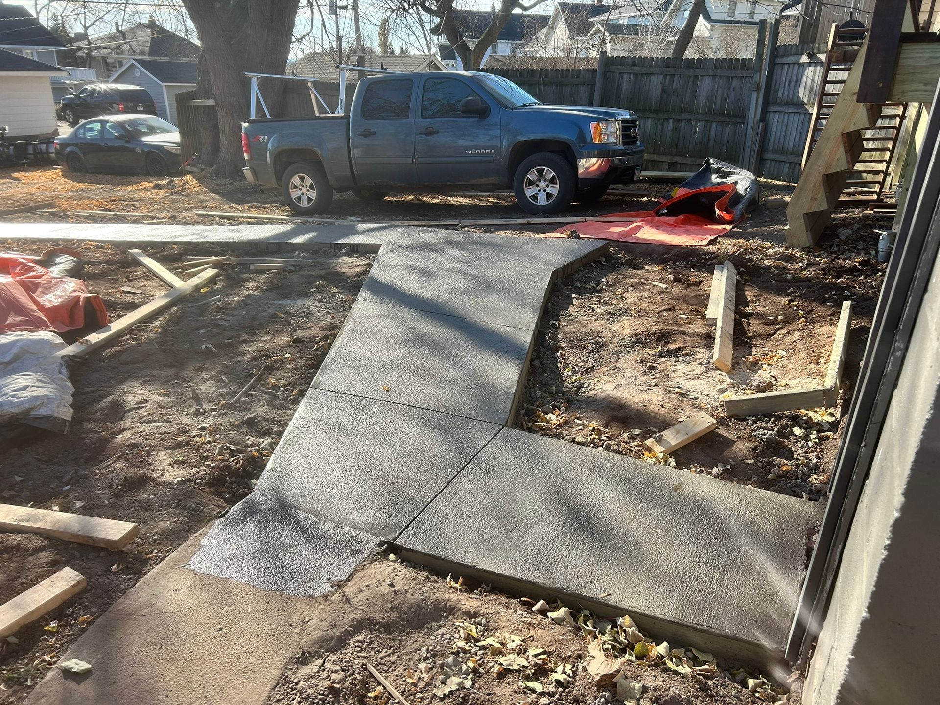 A newly poured concrete walkway in a yard with a truck parked in the background.