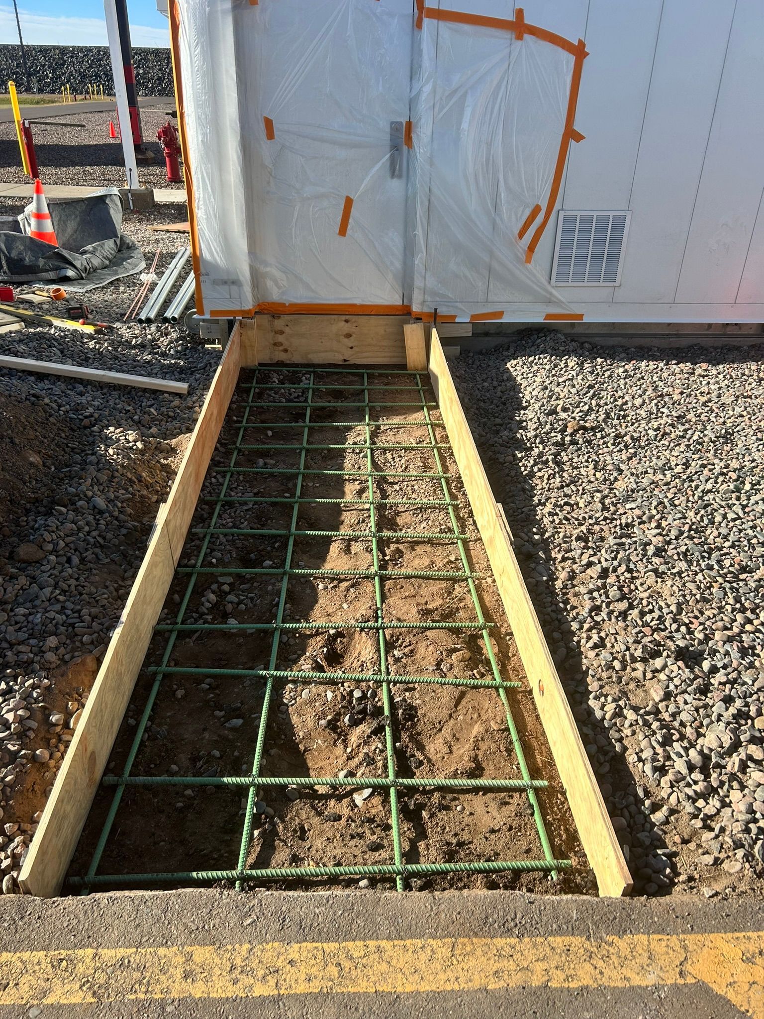 Wooden formwork and a rebar grid prepared for a concrete walkway installation in an outdoor construction area.