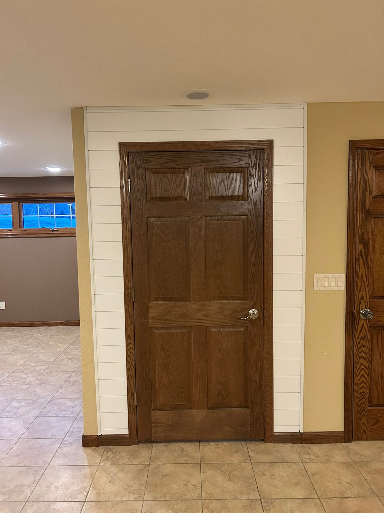 A dark wooden door set in a white shiplap wall, surrounded by beige walls in a tiled room.