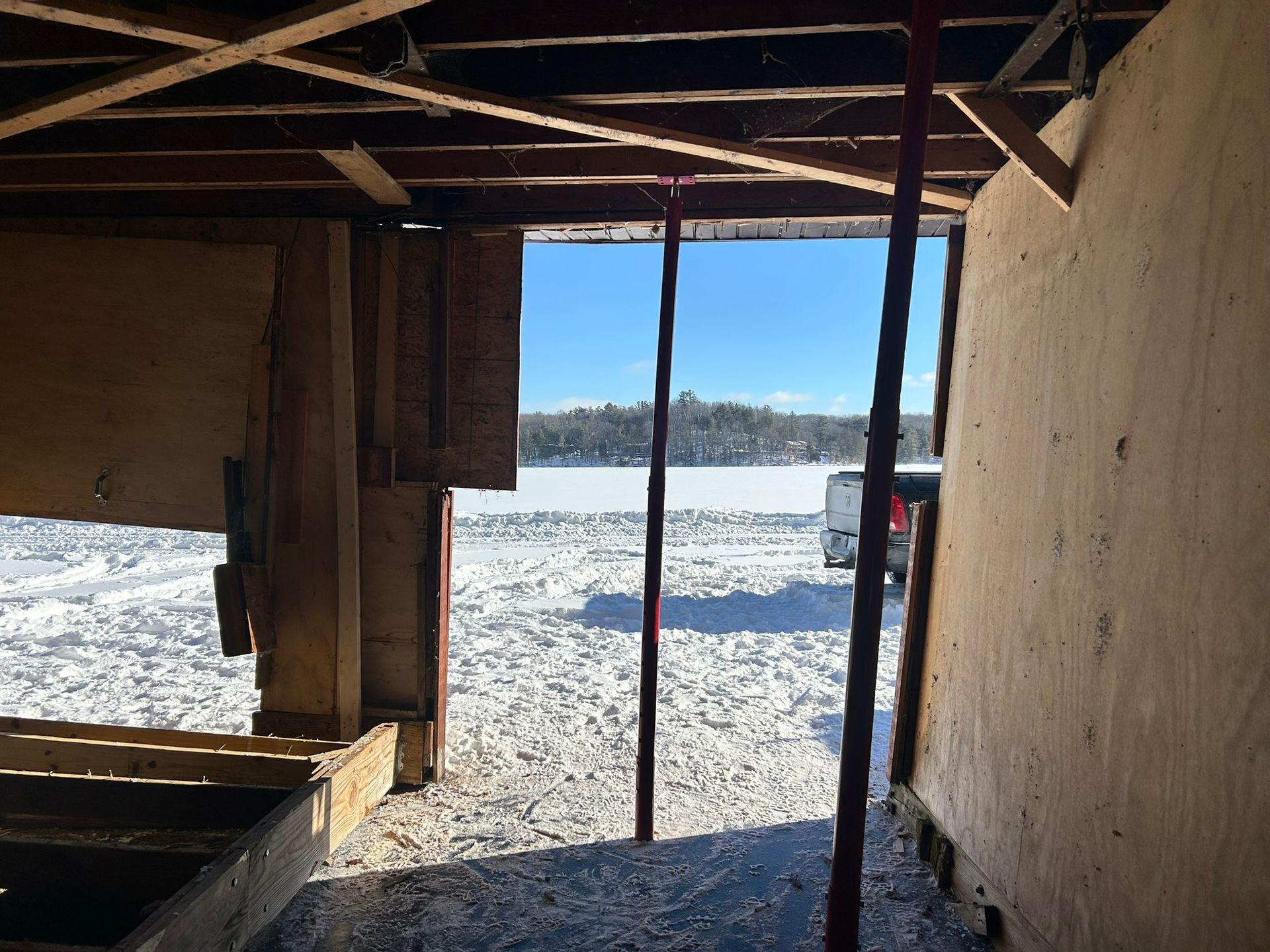 View from inside a rough structure looking out toward a snow-covered frozen lake under a clear blue sky.