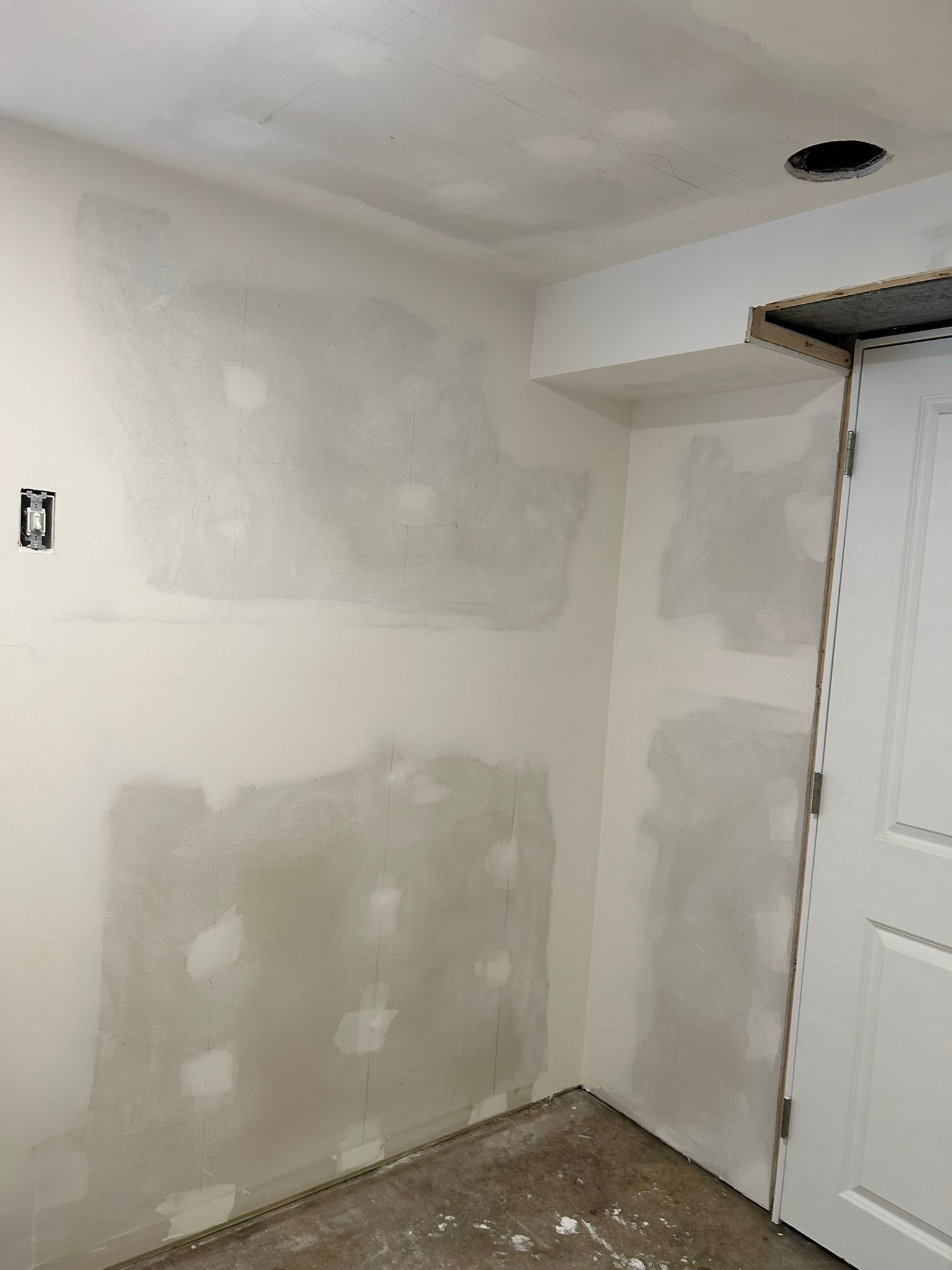 An unfinished interior corner room with drywall patches on the beige walls and ceiling, awaiting paint and finishing.