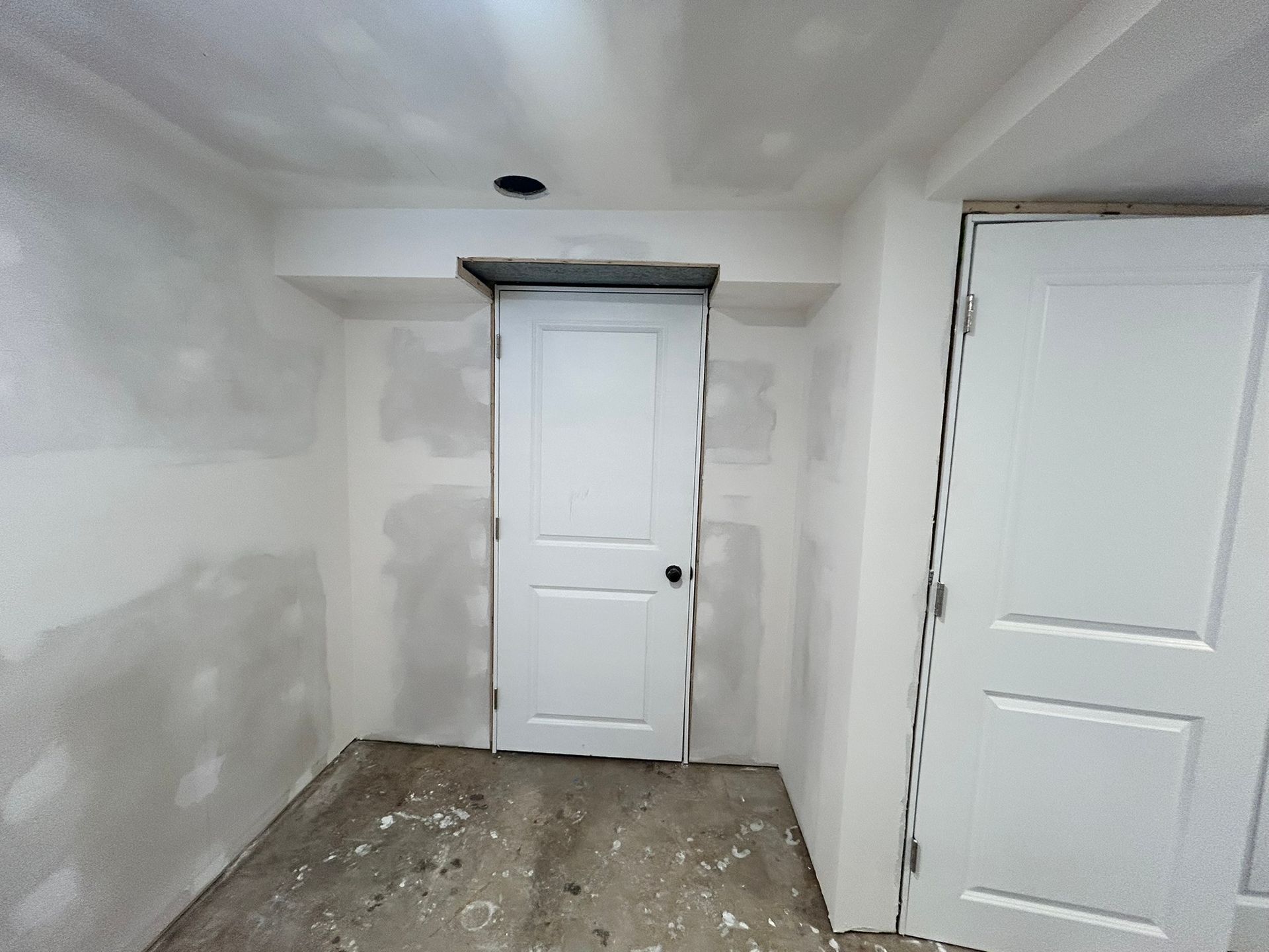 An unfinished room with white drywall, two closed white interior doors, and an exposed ceiling patch.