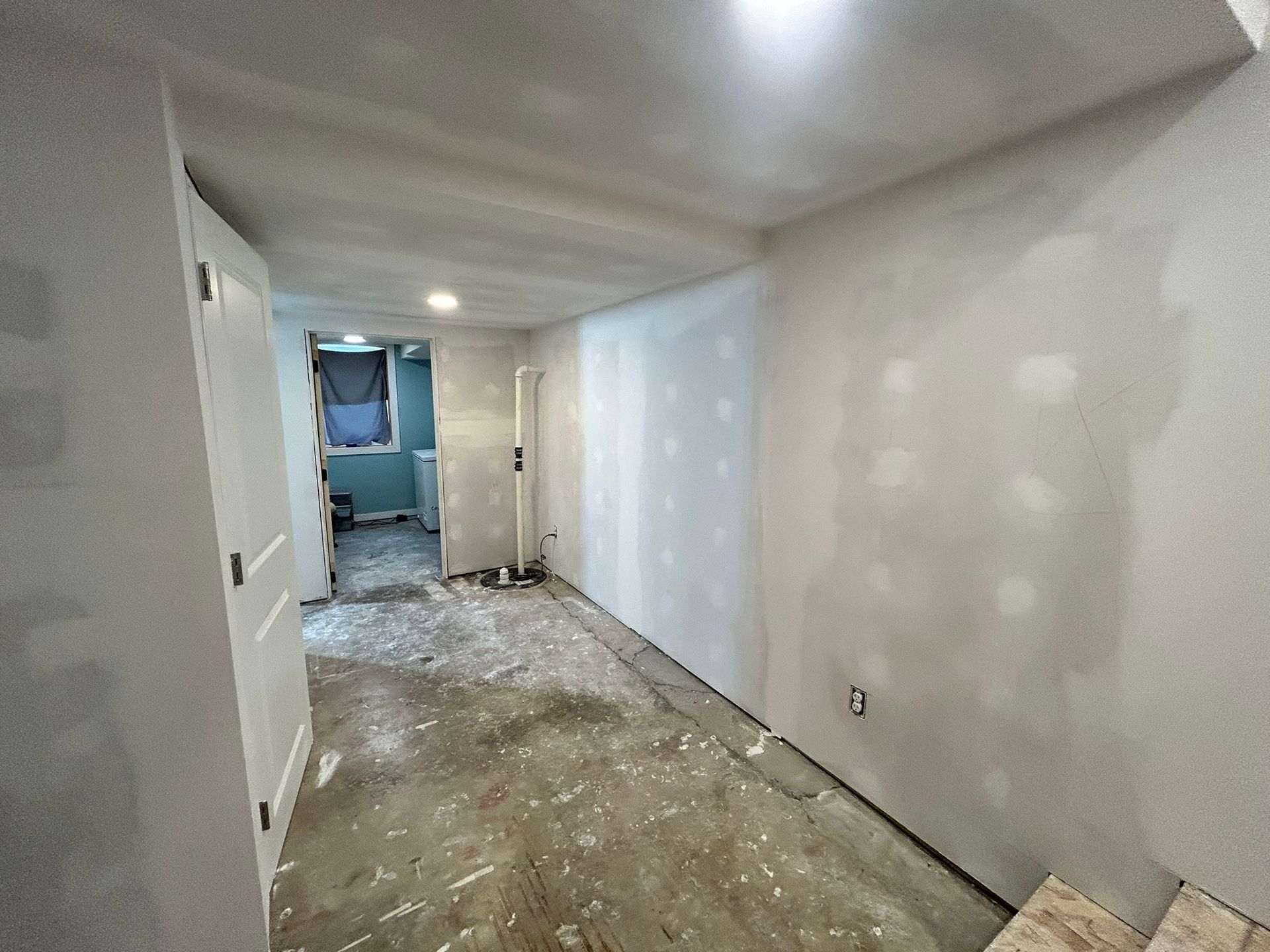 A room under construction with freshly installed white drywall, patch-worked seams, and an unfinished concrete floor.