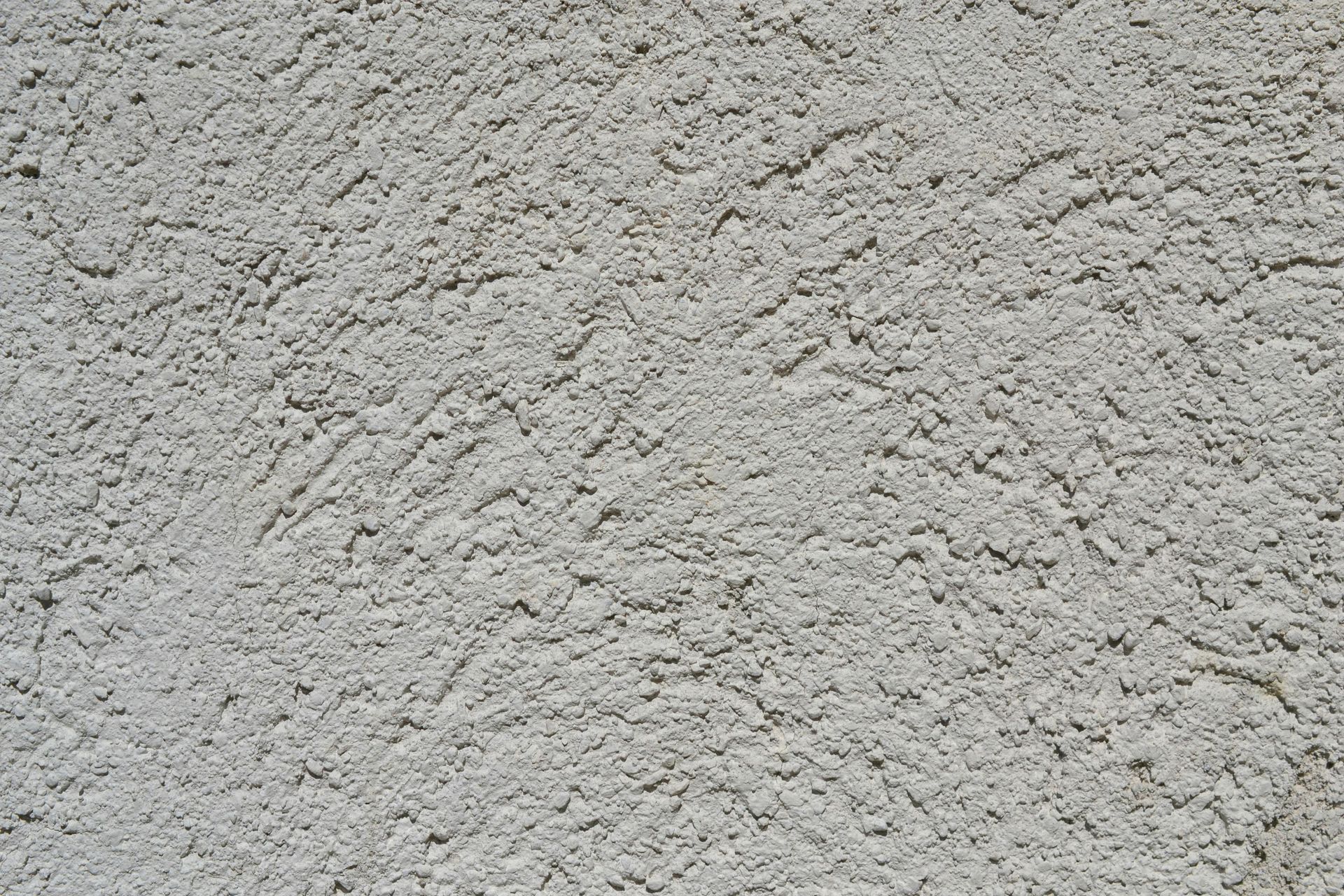 A close-up of a light gray, rough-textured stucco or plaster wall surface.