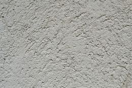 A close-up of a light gray, rough-textured stucco or plaster wall surface.