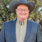 A man in a suit and cowboy hat is smiling for the camera.