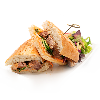 Sliced sandwich, pork, vegetables, with side salad on a white plate.