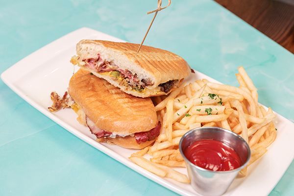 Cuban sandwich cut in half, french fries, and ketchup on a white platter.