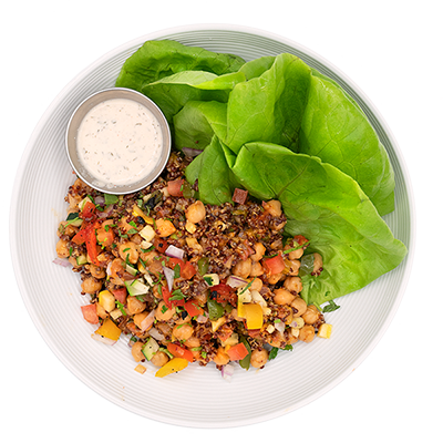 Salad with chickpeas, vegetables, and dressing on a plate with lettuce leaves.