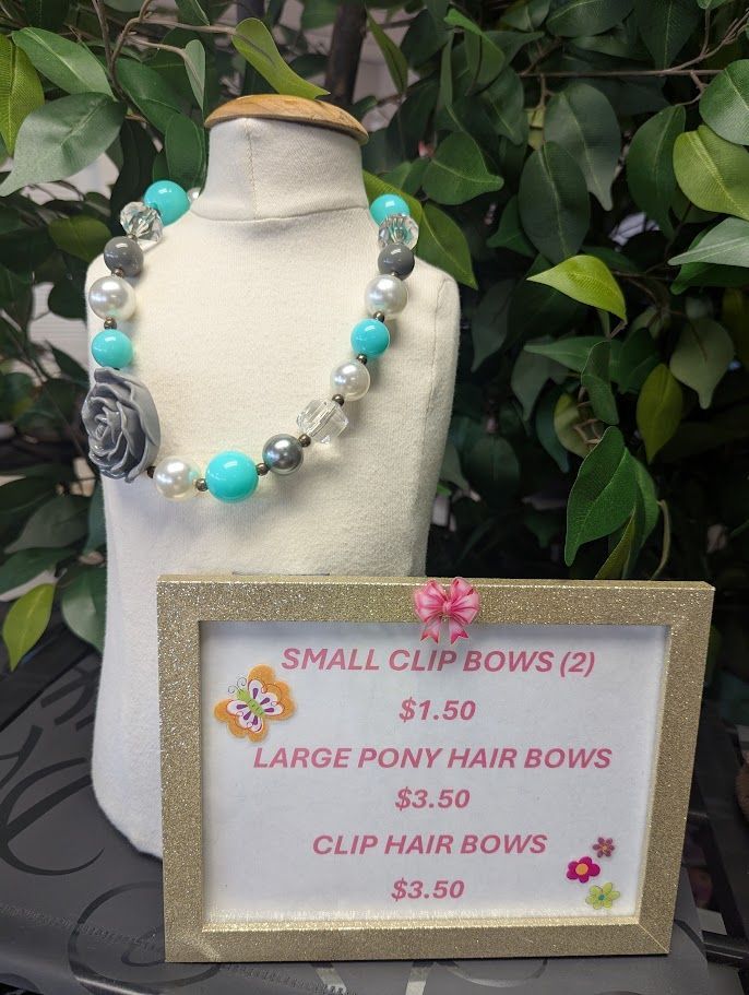 A mannequin with a necklace and a sign that says small clip bows and large pony hair bows