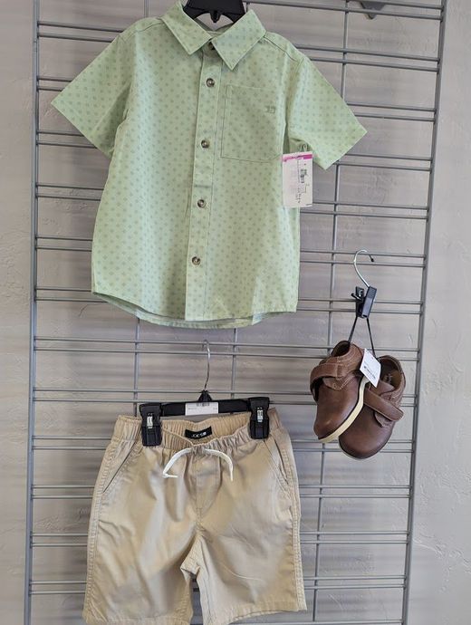 A green shirt , khaki shorts , and brown shoes are hanging on a rack.
