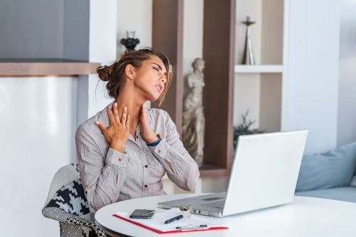 Woman at laptop, holding neck in pain, sitting at table.