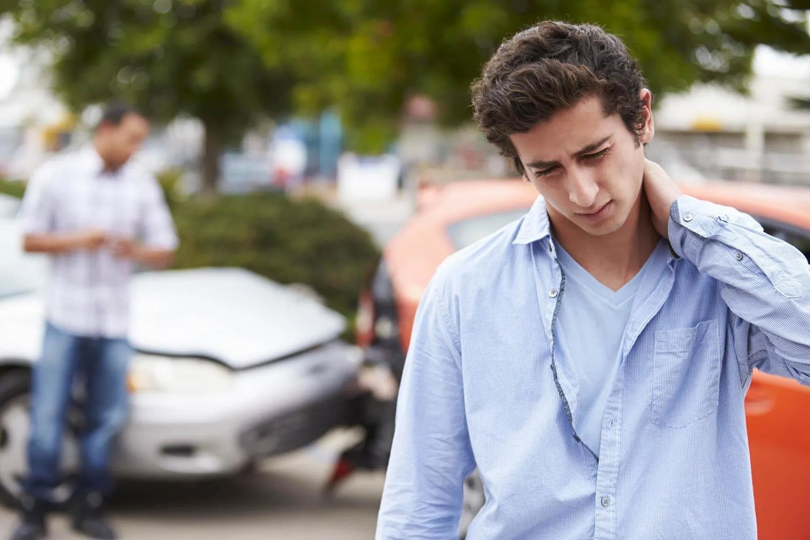 A man is holding his neck in pain in front of a car accident.