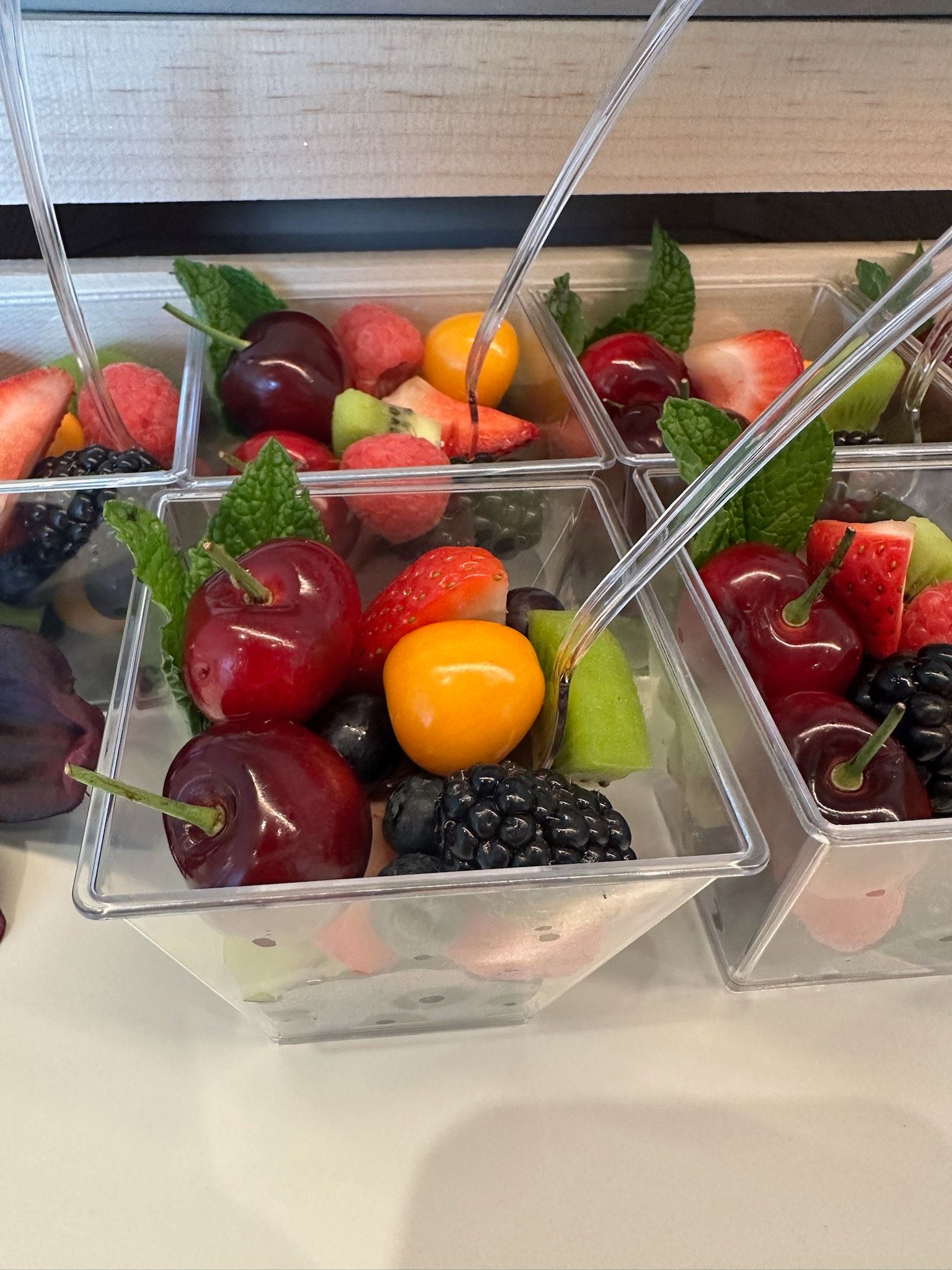 Fruit salad cups with cherries, berries, kiwi, and mint, in clear plastic containers.