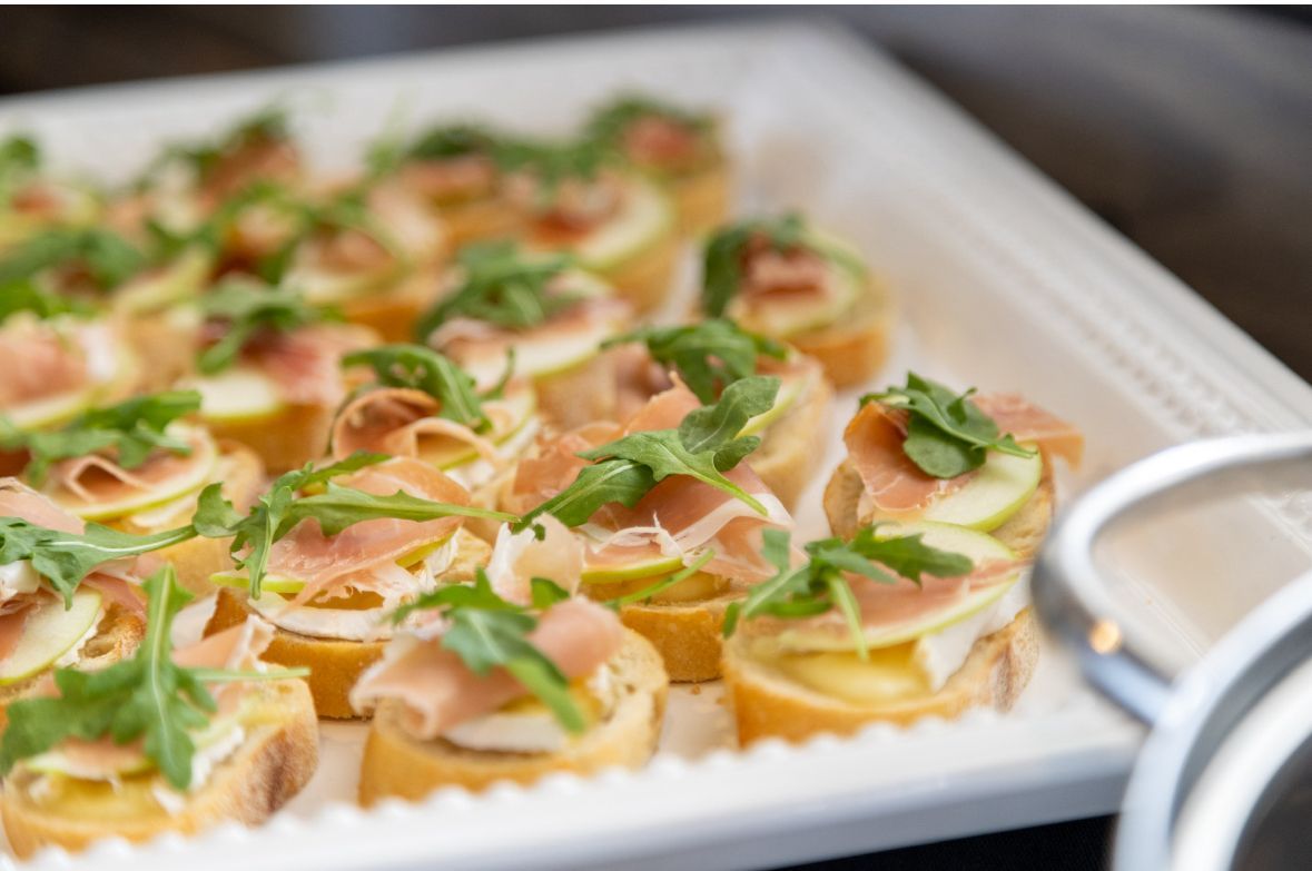 Tray of appetizers: baguette slices topped with fig, prosciutto, and arugula.