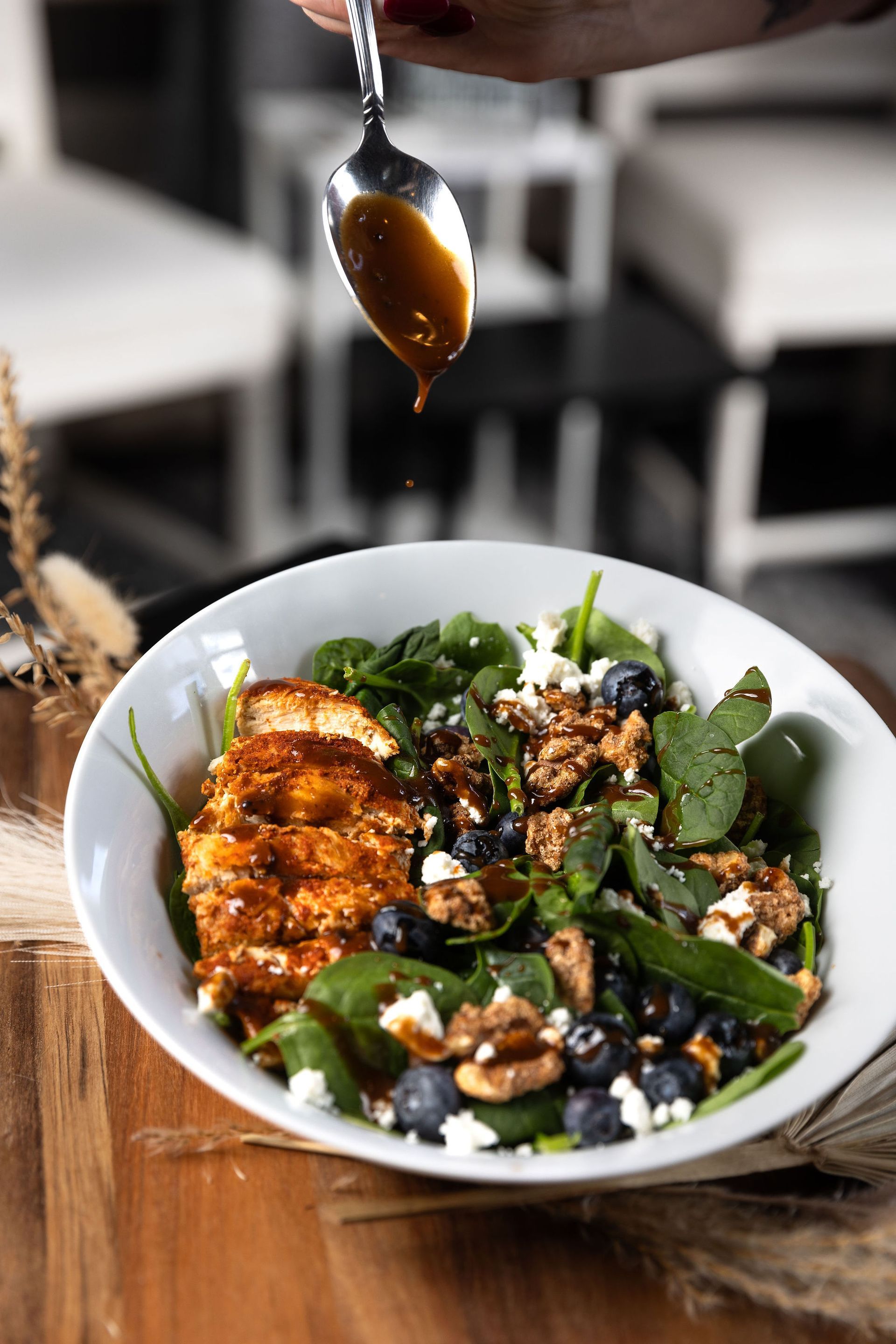 Salad bowl with spinach, blueberries, cheese, and chicken being drizzled with sauce.