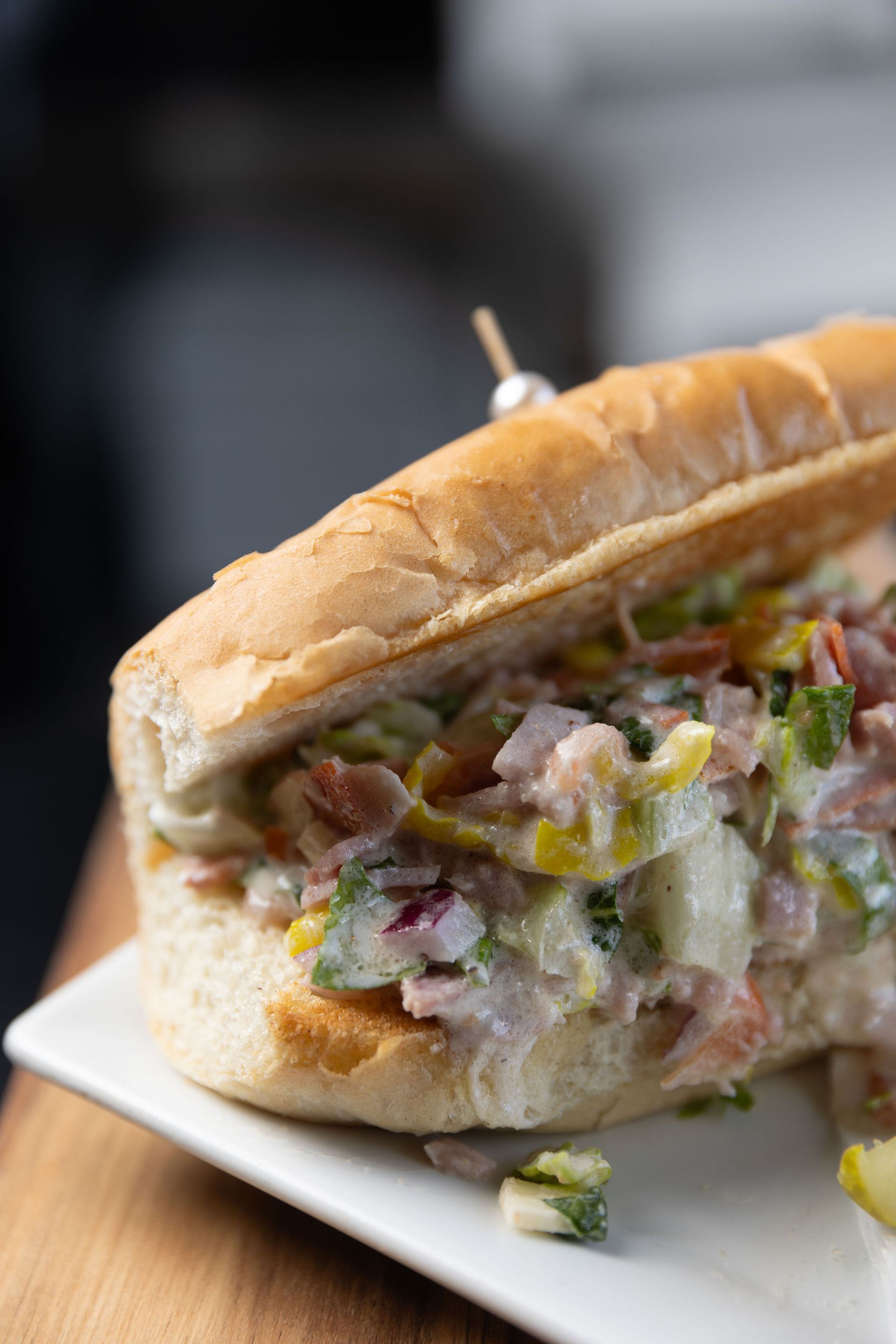 Sub sandwich on white plate; filled with creamy salad, topped with a toothpick.