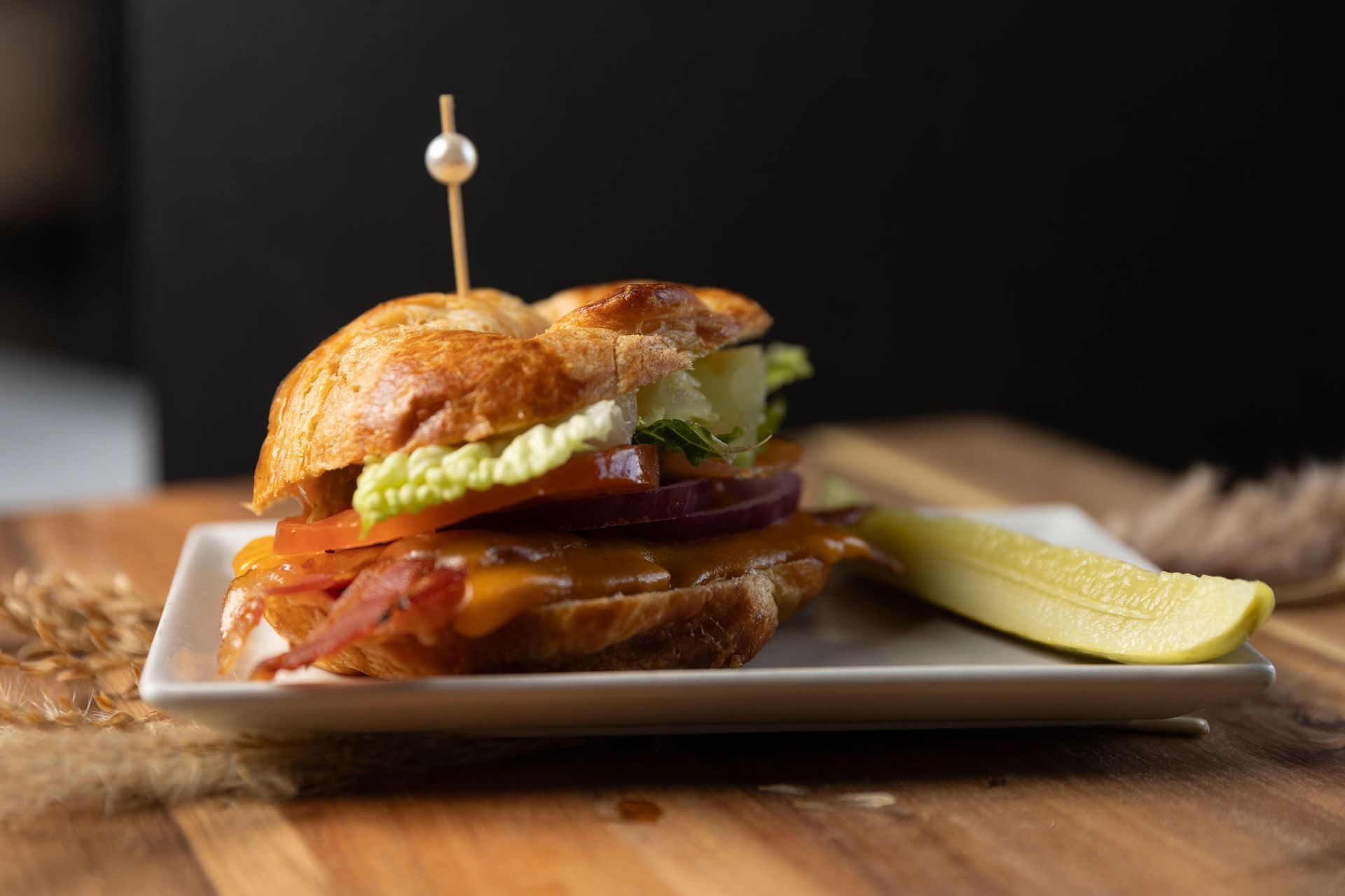 Sandwich with lettuce, tomato, and onion on a plate with a pickle and a skewer.