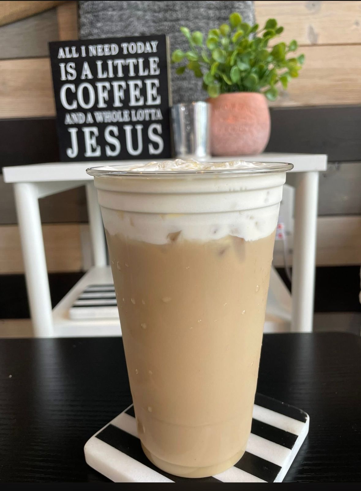 Iced drink in clear plastic cup with ice, next to a dark flower and white flower.