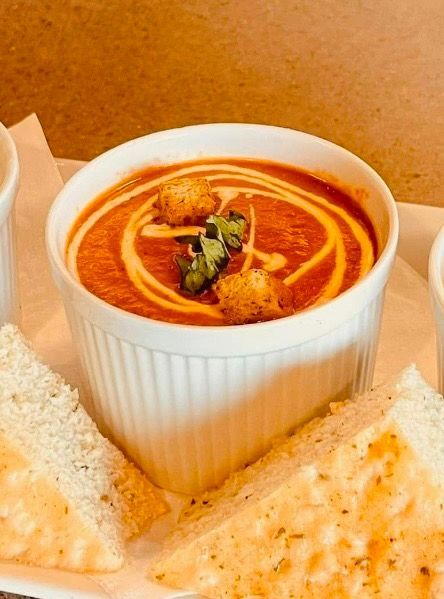 Tomato soup in white bowl, swirled with cream, topped with croutons and herbs; served with toasted bread.