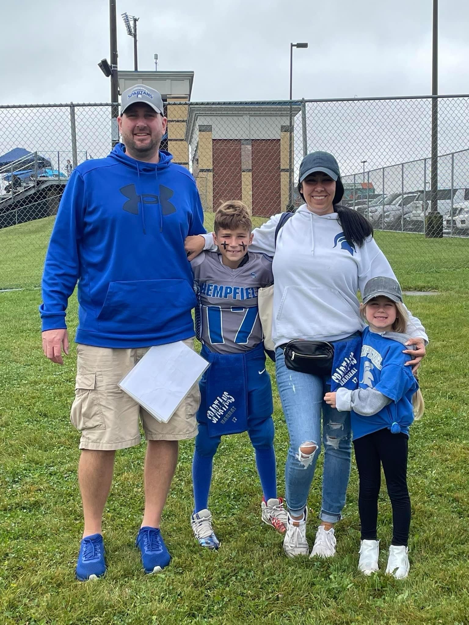 Family of four in blue and white standing on a grassy field, posing for a photo.