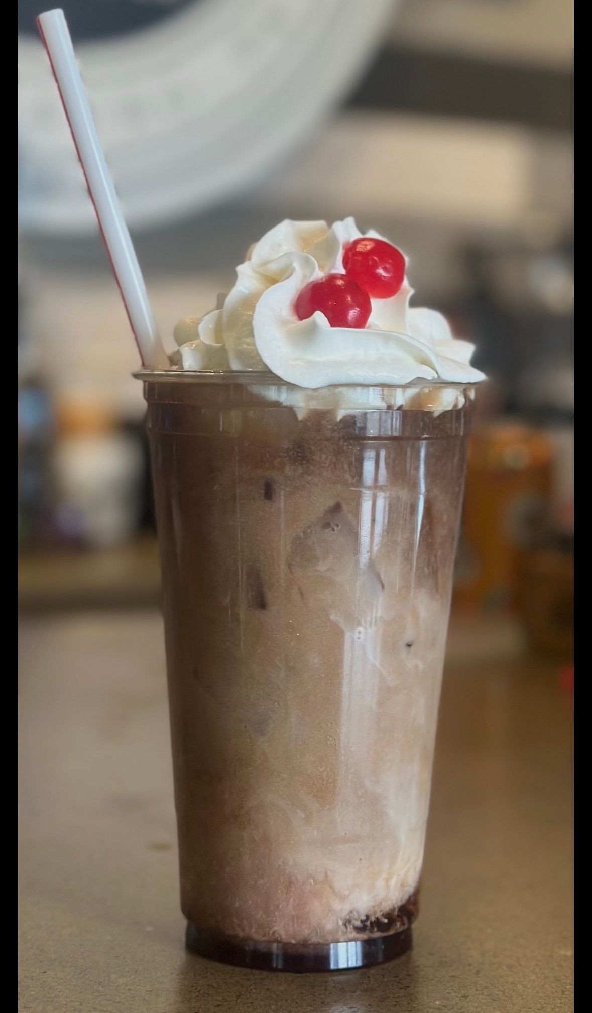 Chocolate milkshake with whipped cream and cherry in a clear cup with straw.