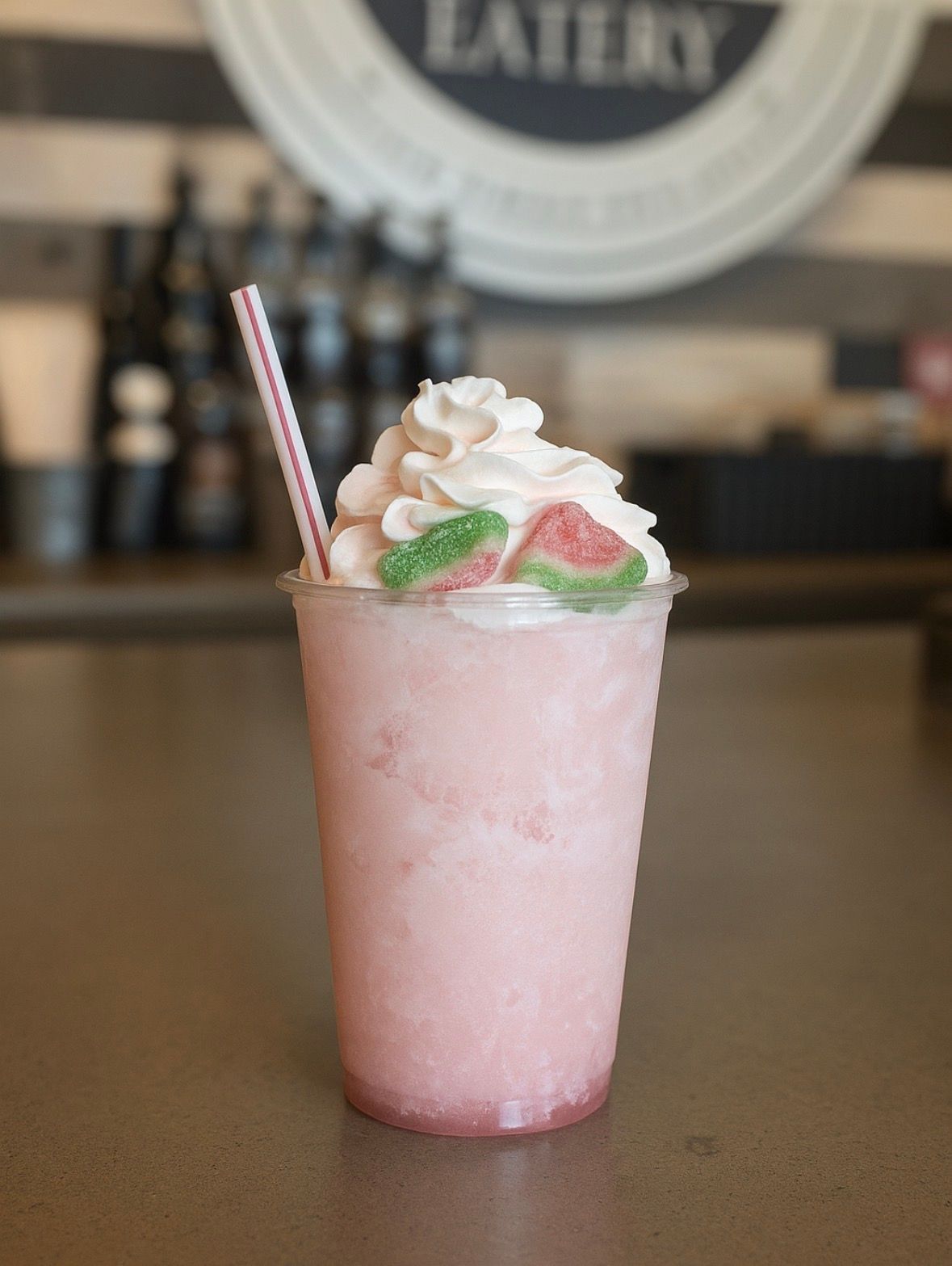 Pink slushy drink in a clear cup, topped with whipped cream and candy, with a straw.