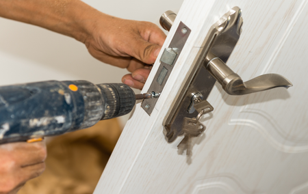 Person using a power drill to install a door lock on a white door.